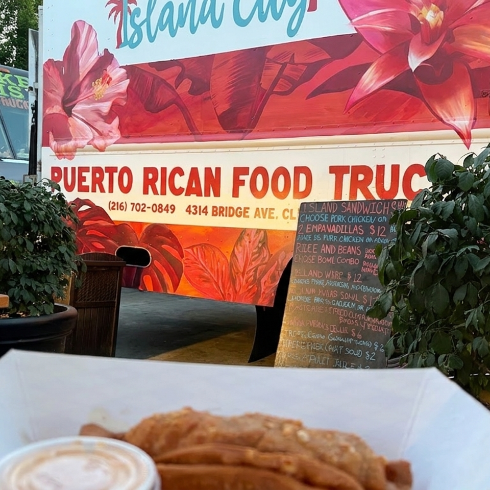Puerto Rican food truck with colorful floral artwork, outdoor seating, menu board, and fried food with dipping sauce in the foreground.